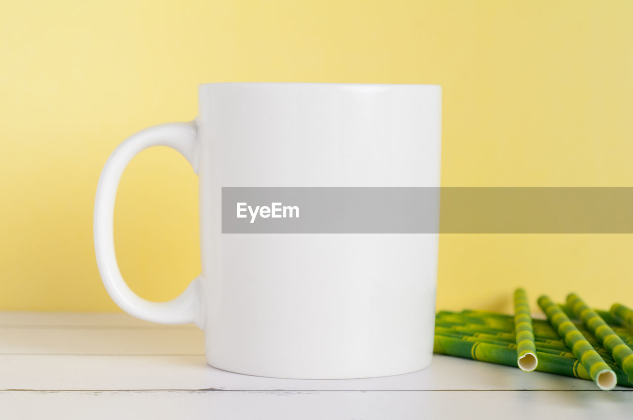 CLOSE-UP OF TEA CUP ON TABLE AGAINST YELLOW BACKGROUND