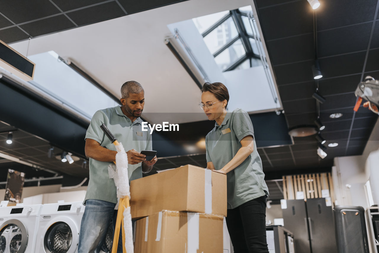 Low angle view of multiracial male and female sales clerks discussing over calculator at appliances store