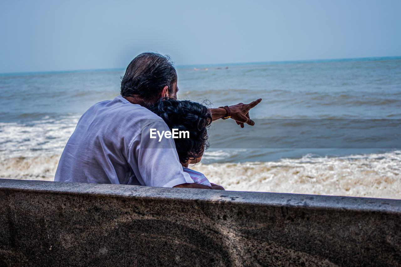 Grandfather with granddaughter looking at sea while sitting on bench