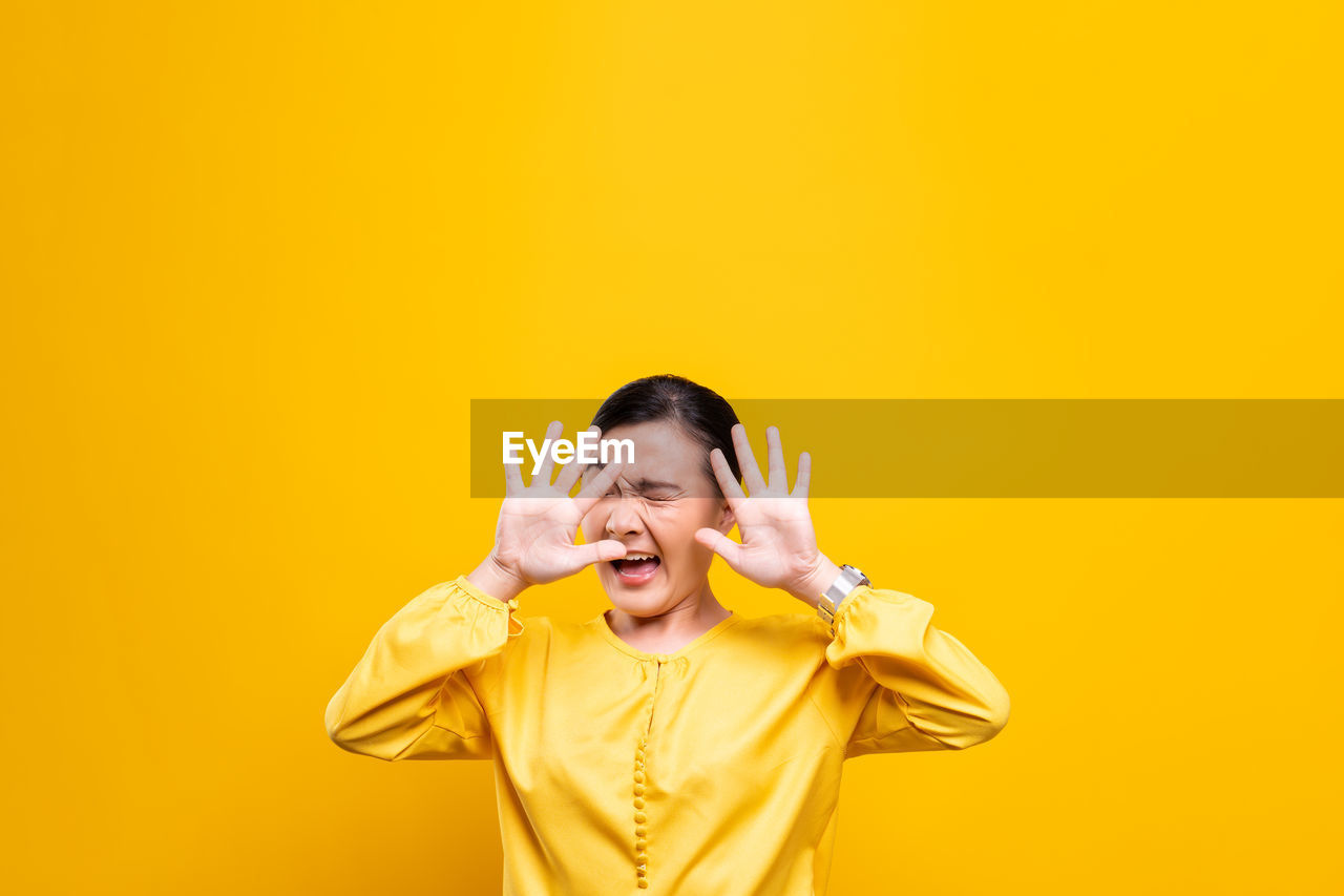 Woman showing stop gesture while standing against yellow background