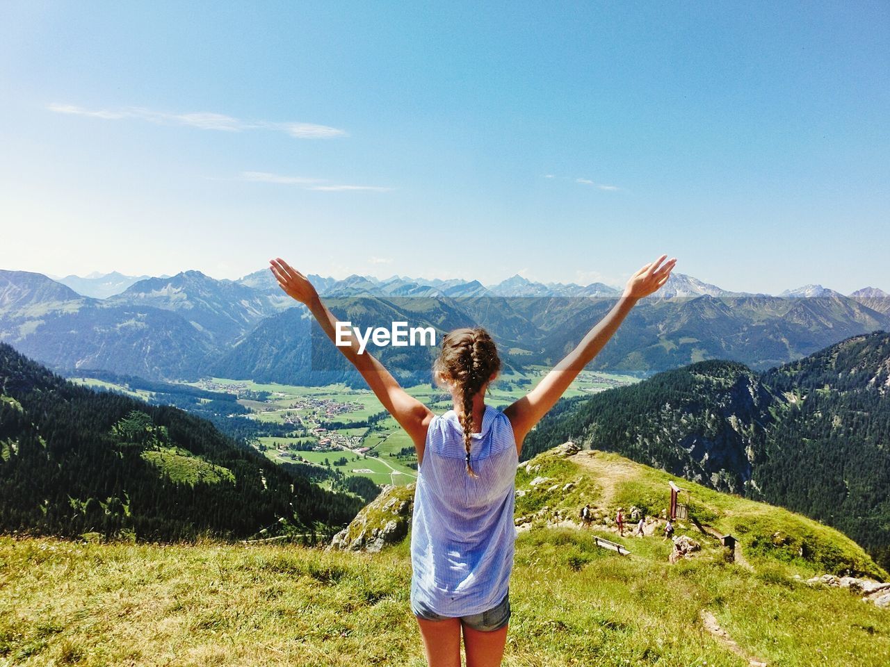 Rear view of young woman with arms raised standing on mountain against sky