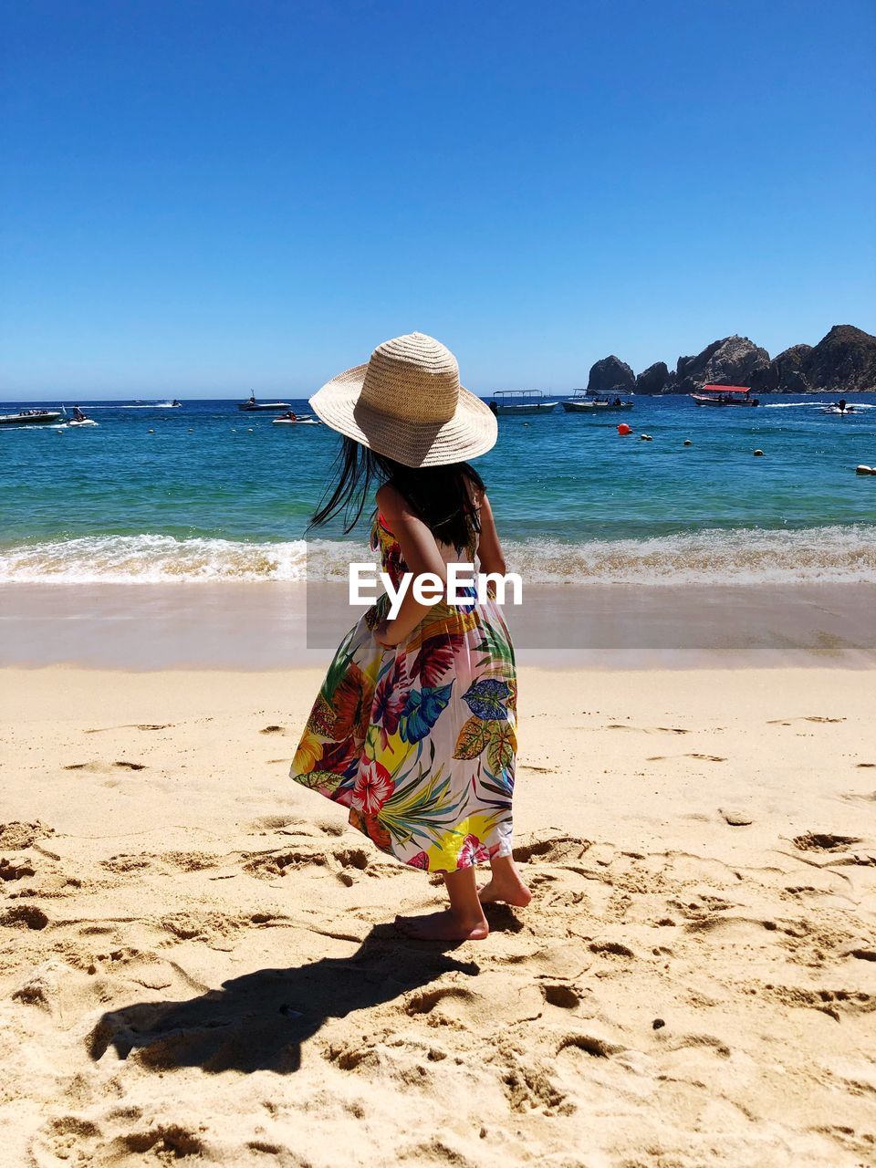 Full length of girl wearing hat standing at beach against clear sky