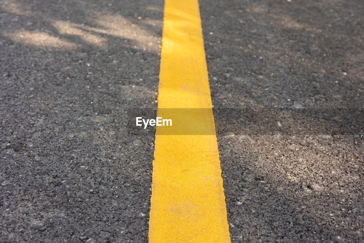 Yellow line on concrete road with rough surface under sunlight in the park shows concept of sign 