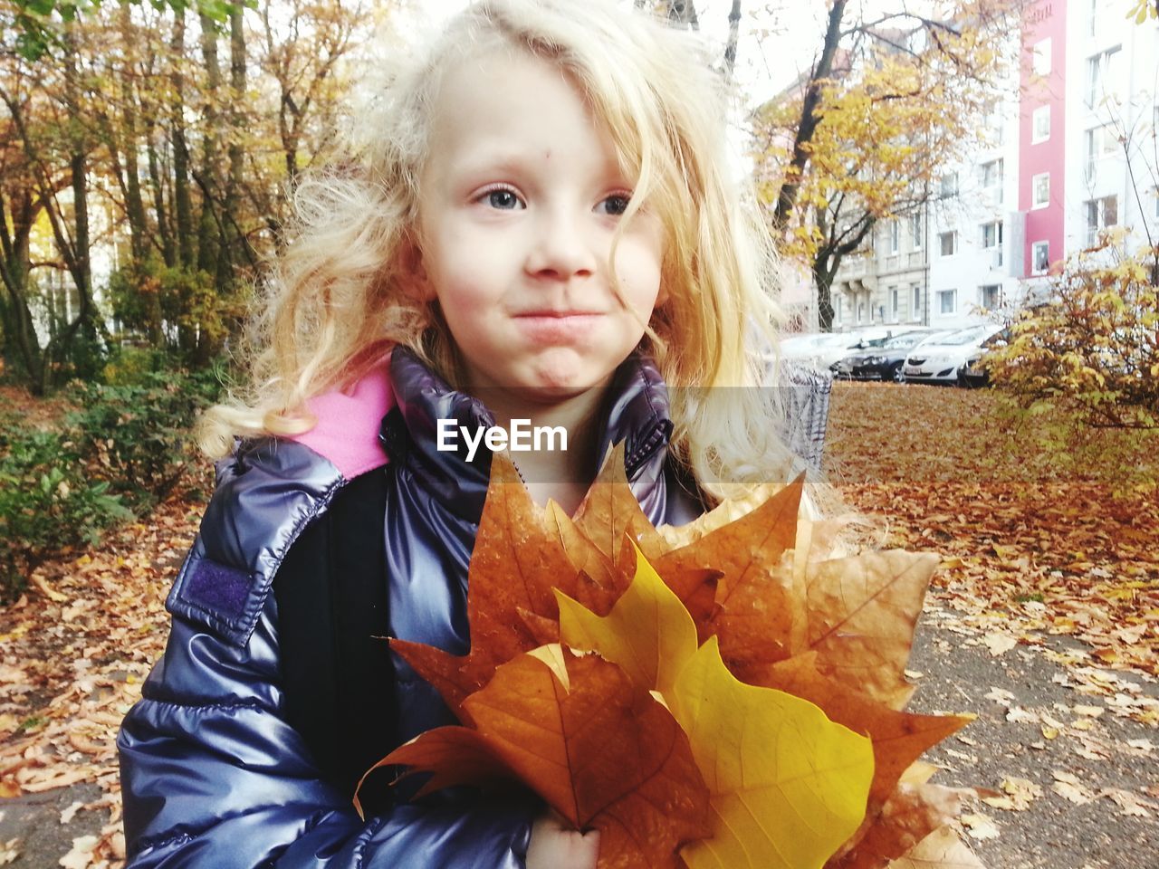 Blond girl making face with autumn leaves