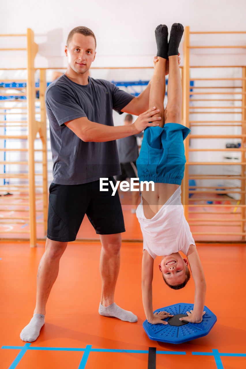 Balance exercises for children, child doing a hand stand with trainer