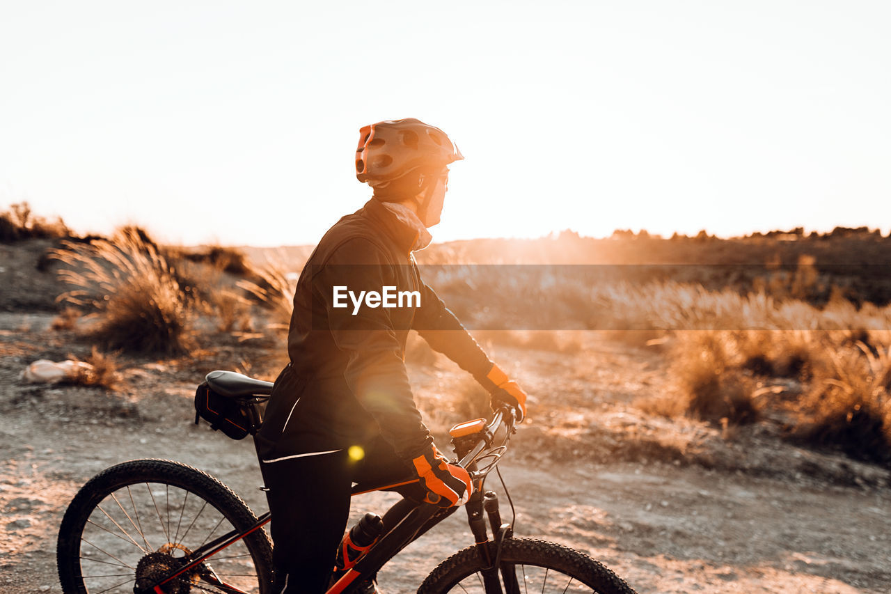 Side view of man riding bicycle on land against sky