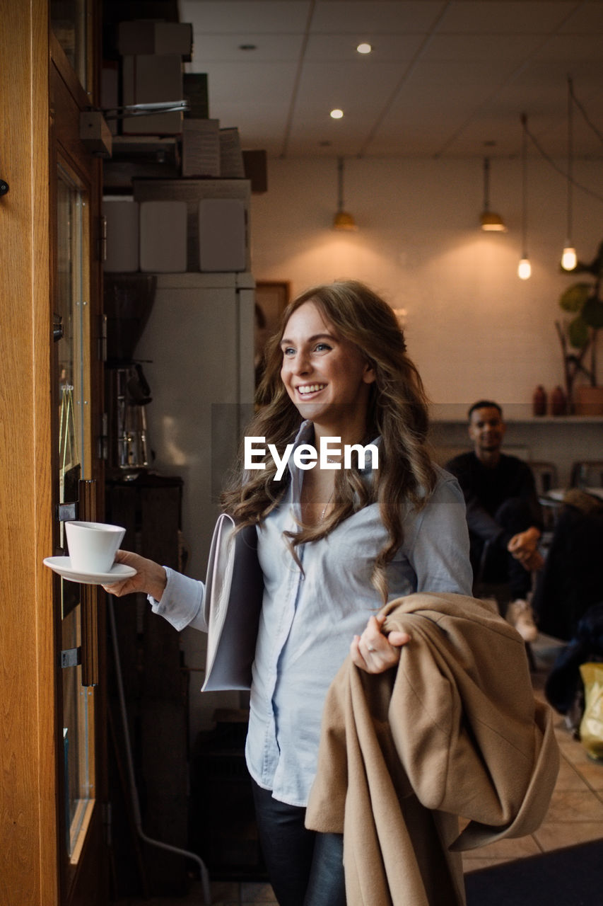 Happy young woman walking with coffee cup and overcoat at cafe