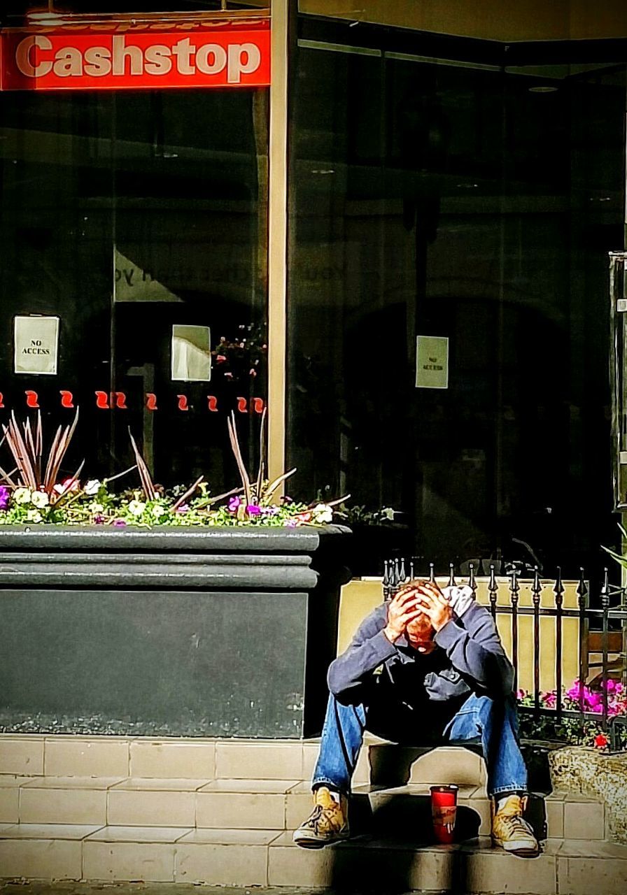 MAN SITTING ON SIDEWALK