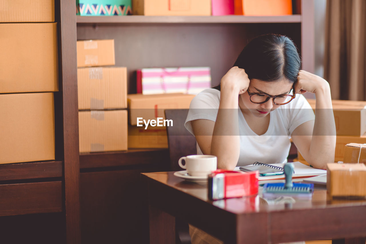 Sad young woman sitting by objects on table