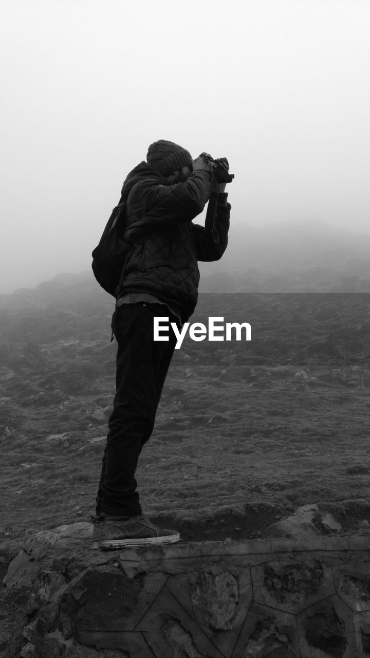 REAR VIEW OF MAN STANDING ON MOUNTAIN LANDSCAPE