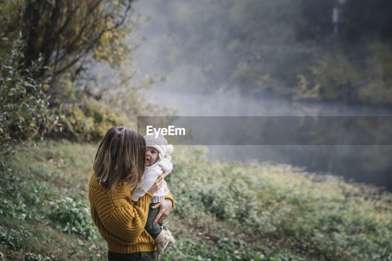 A woman is holding a baby near a river