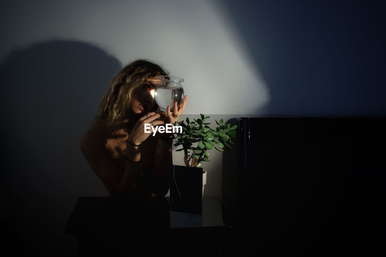 Young woman holding vase with water in darkroom at home