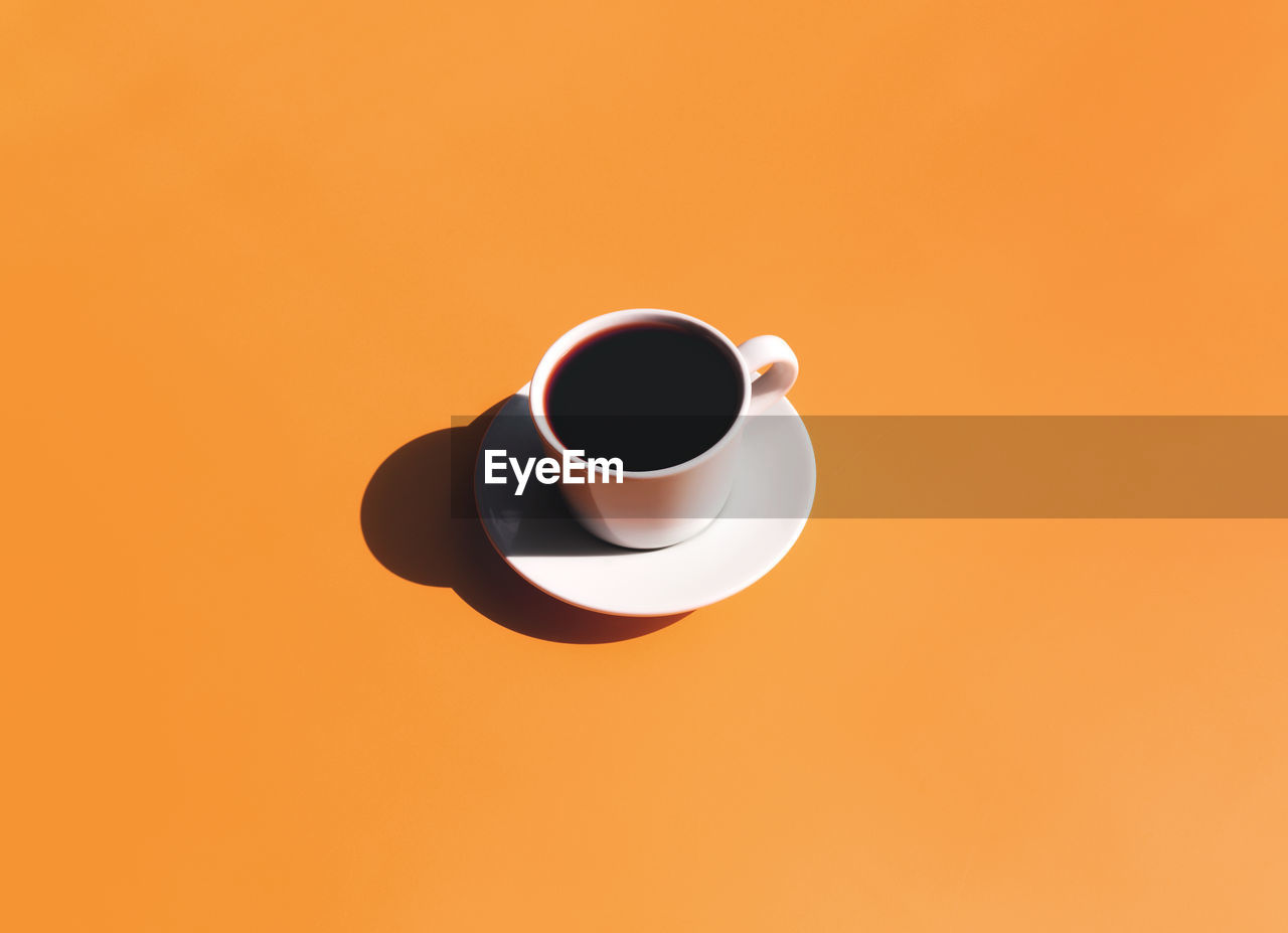 HIGH ANGLE VIEW OF COFFEE CUP AGAINST ORANGE BACKGROUND