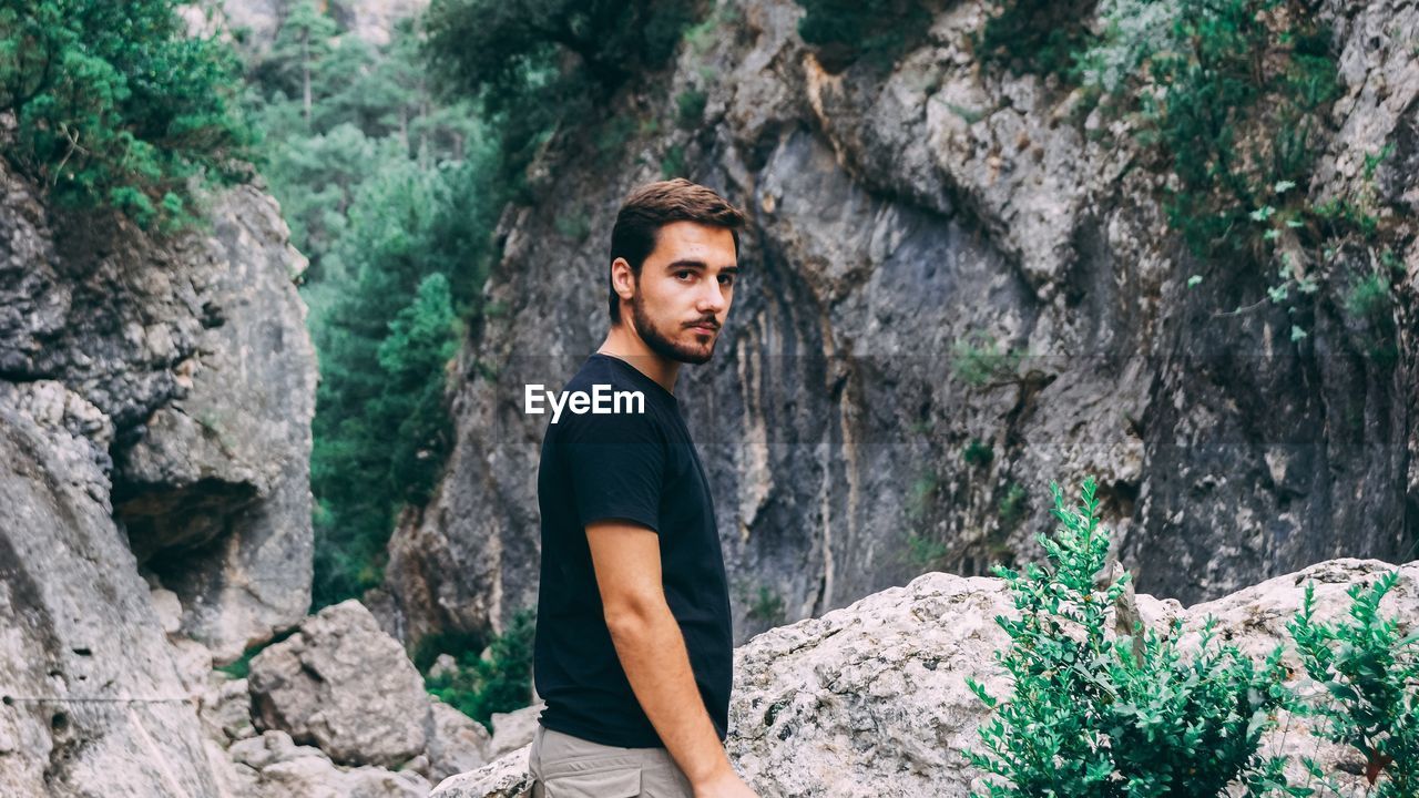 Portrait of young man standing against rocks