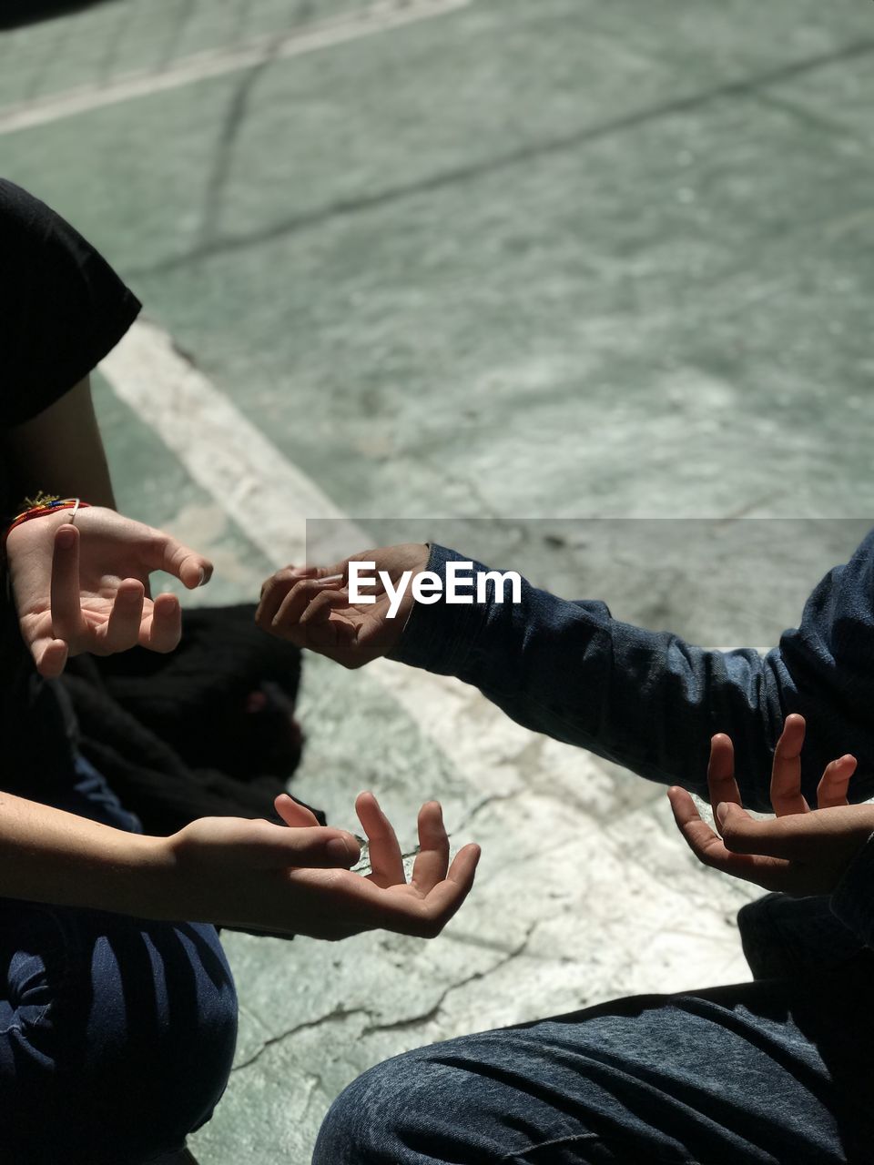 Cropped hands of friends gesturing while sitting on road