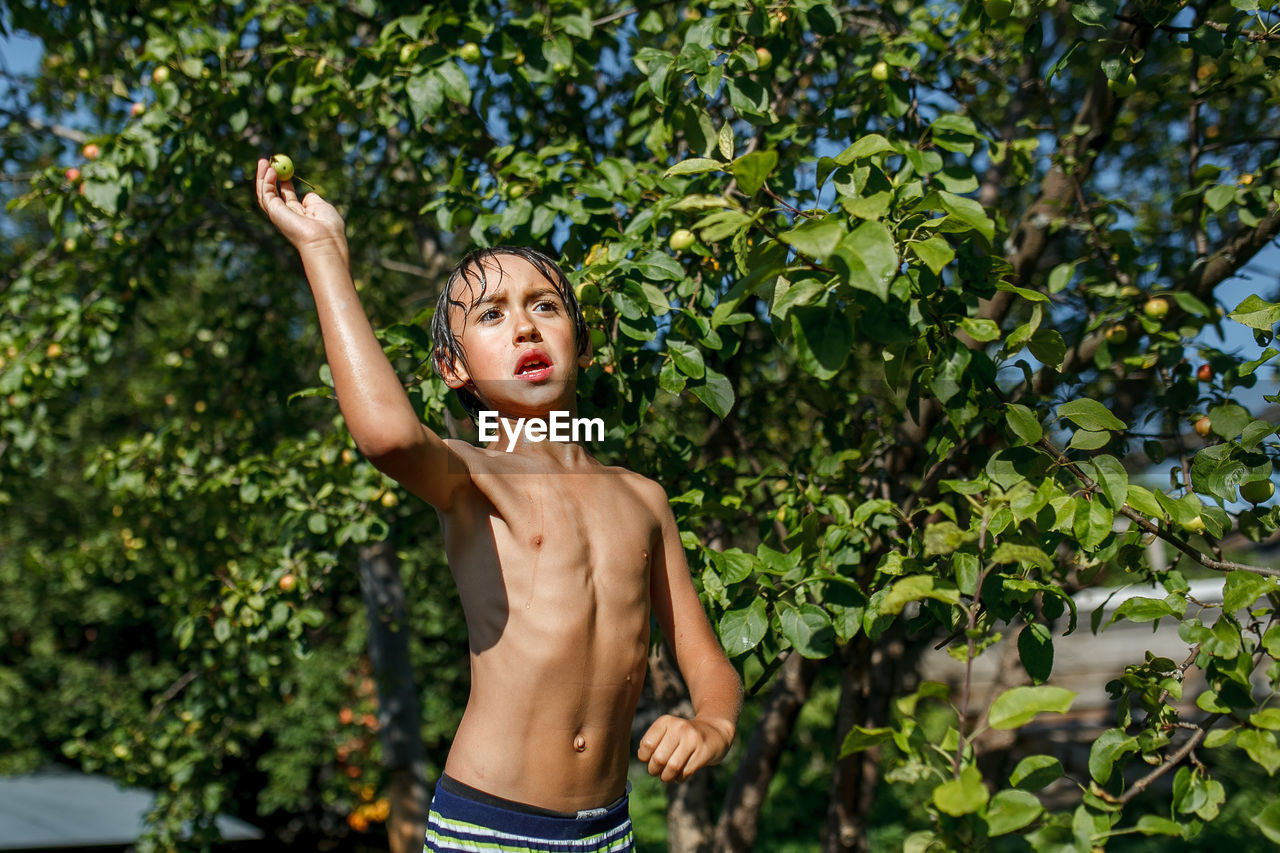 Shirtless boy standing against tree
