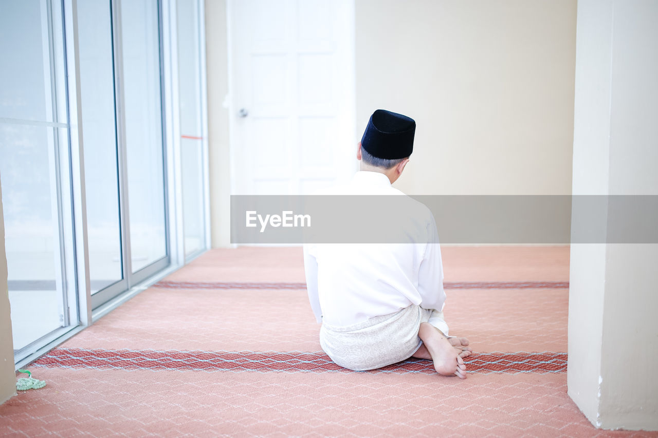 Rear view of man praying in room