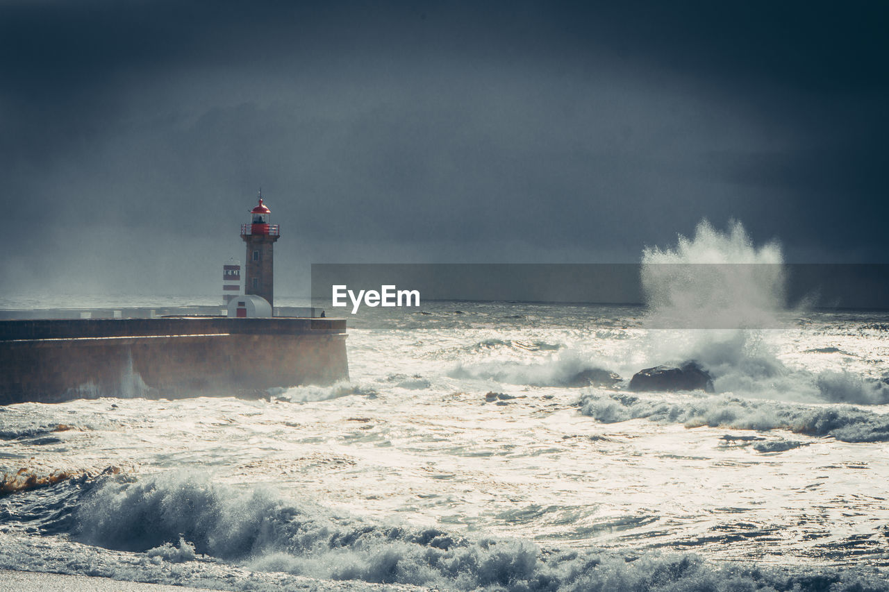 lighthouse, ocean, sea, wave, water, guidance, tower, sky, wind wave, cloud, beach, architecture, motion, coast, nature, land, protection, built structure, security, shore, storm, building exterior, building, environment, beauty in nature, warning sign, scenics - nature, horizon, outdoors, sign, communication, horizon over water, power in nature, wind, no people, travel, water sports, day, coastline, travel destinations