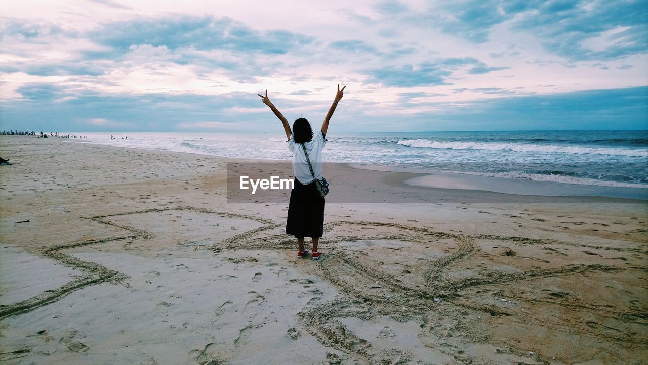 Rear view of woman standing at beach against sky