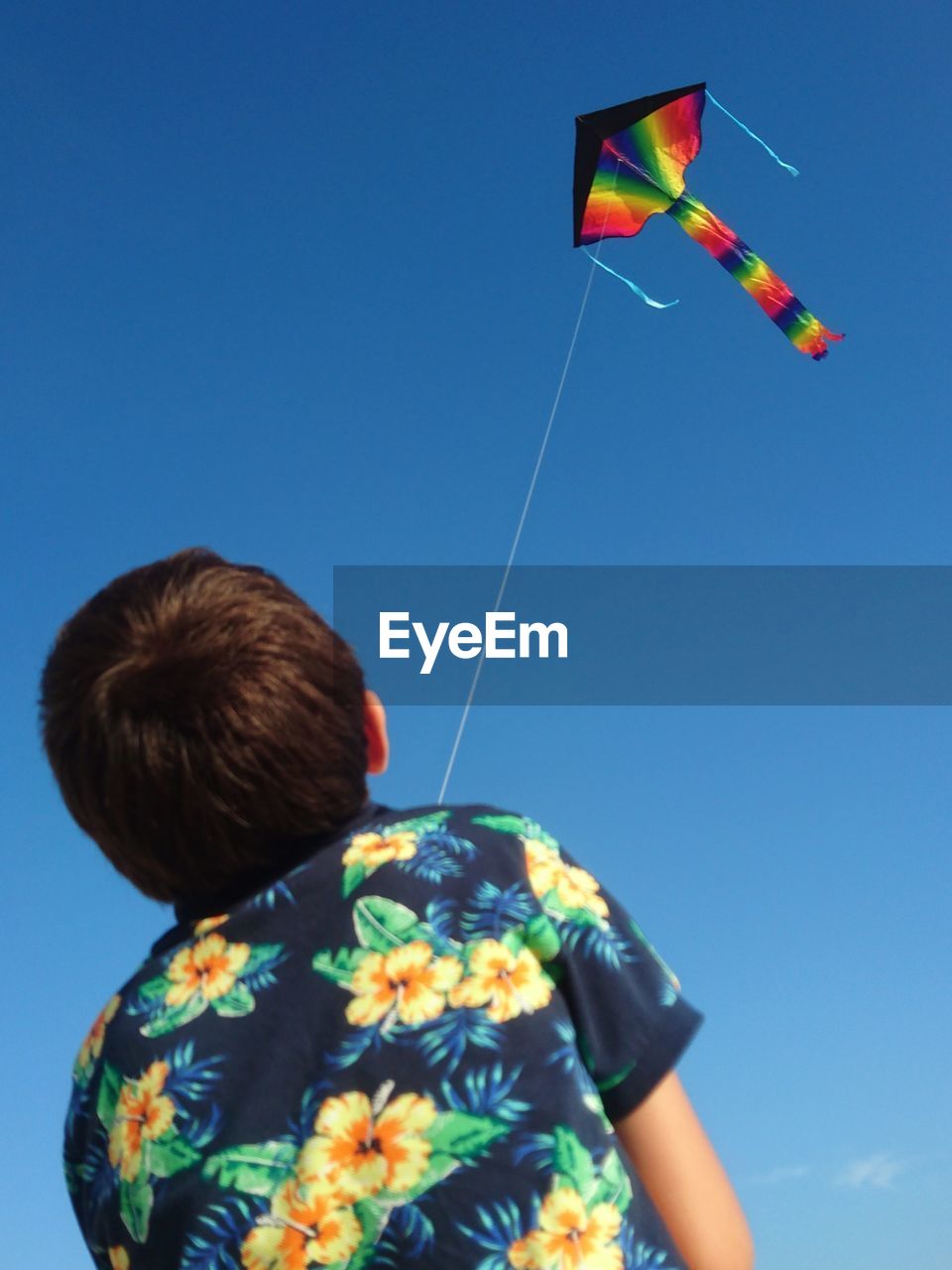 Rear view of boy flying kite while standing against blue sky