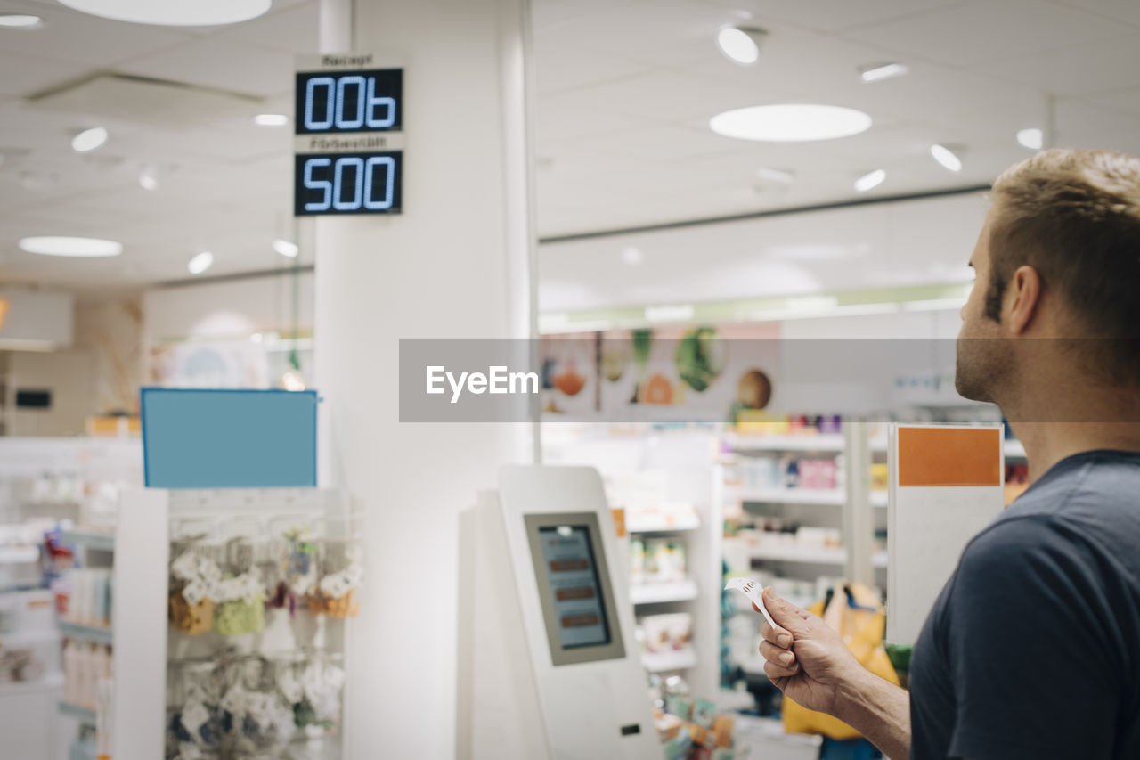 Mature male customer standing with ticket waiting at pharmacy store