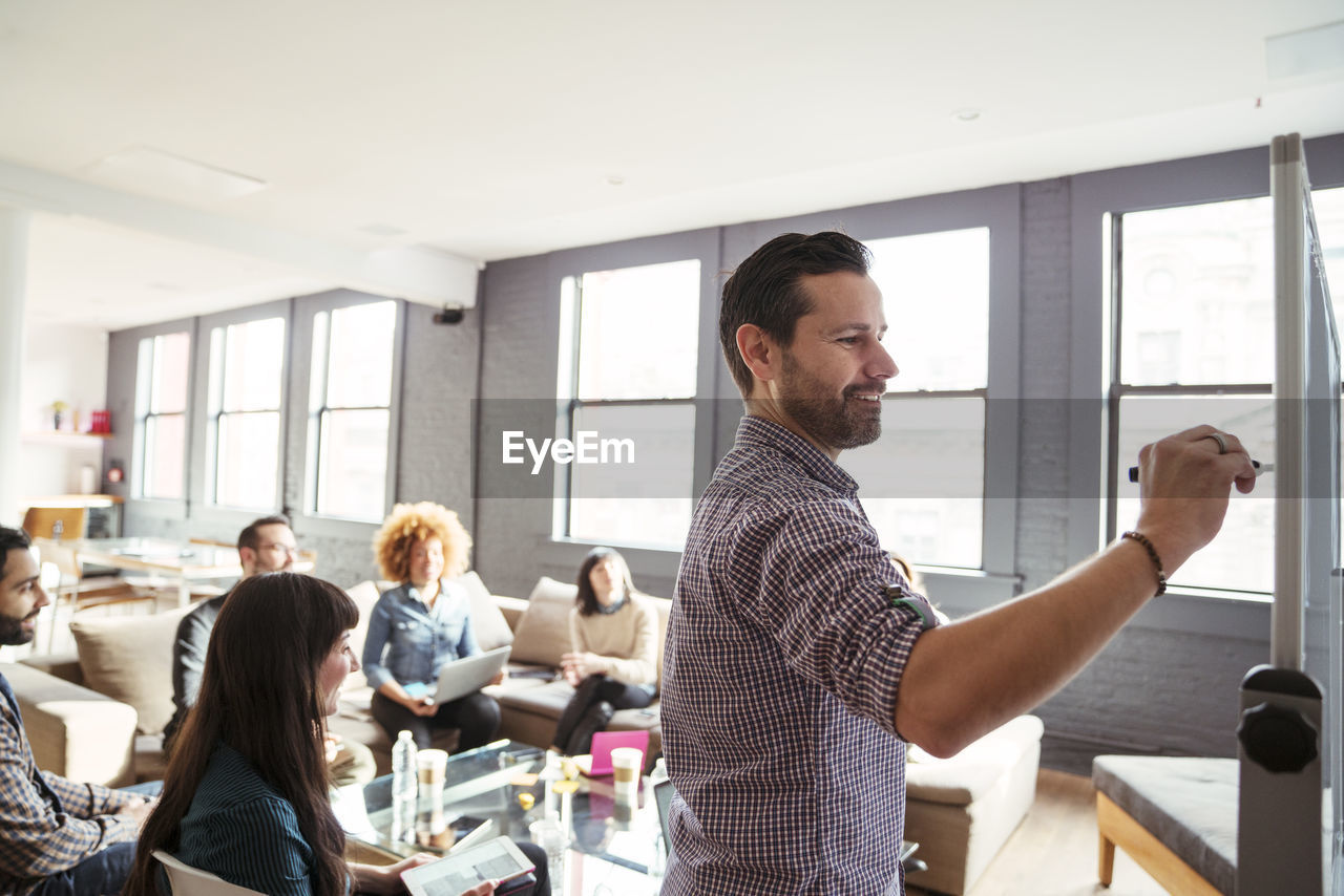 Business people looking at man writing on whiteboard in office