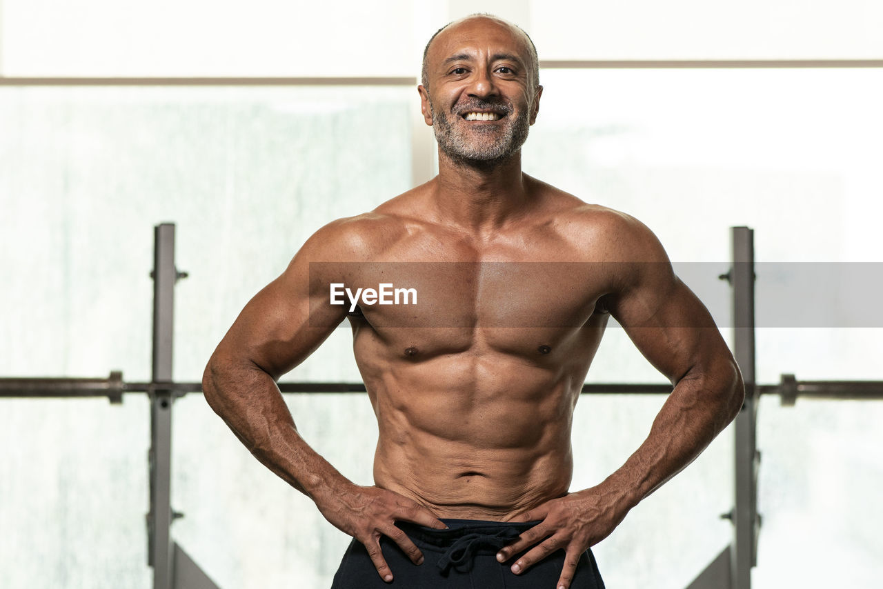 Portrait of shirtless man with hand on hip standing in gym