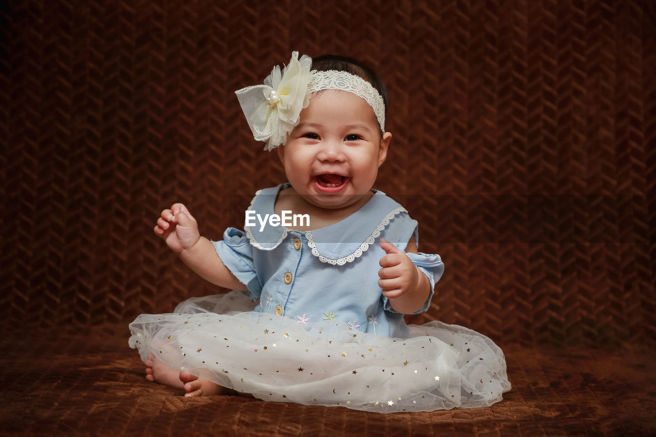 Portrait asian looking toddler white bow headband indoors. sitting happy laughing brown background