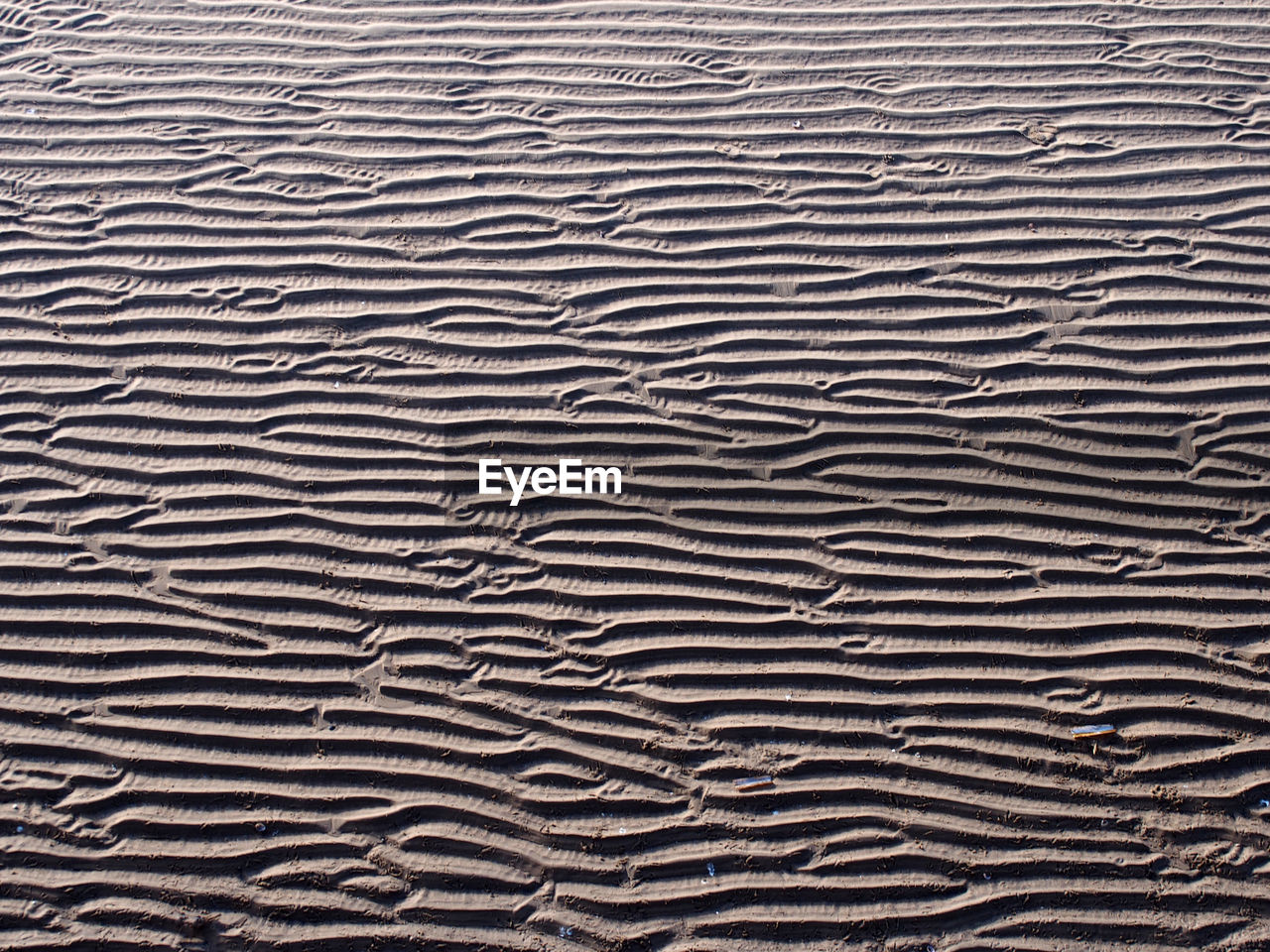 A full frame beach background with wavy pattered surface formed by water on the wet sand