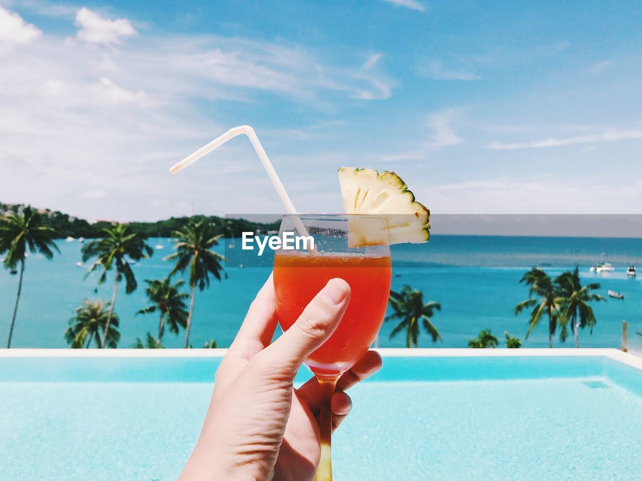 CROPPED IMAGE OF HAND HOLDING DRINK AGAINST THE SEA