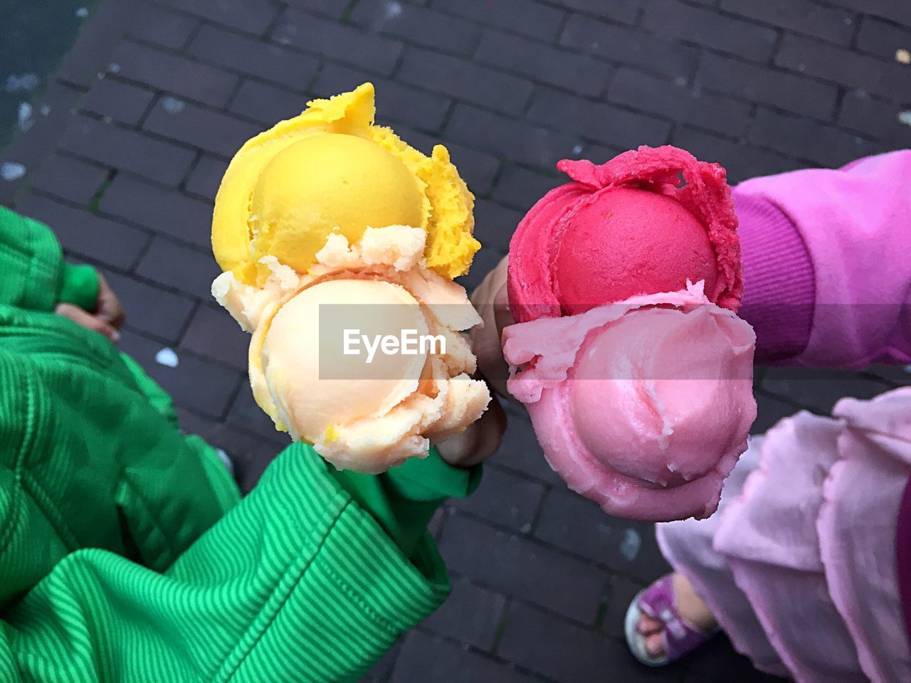 Low section of children holding colorful ice creams on footpath