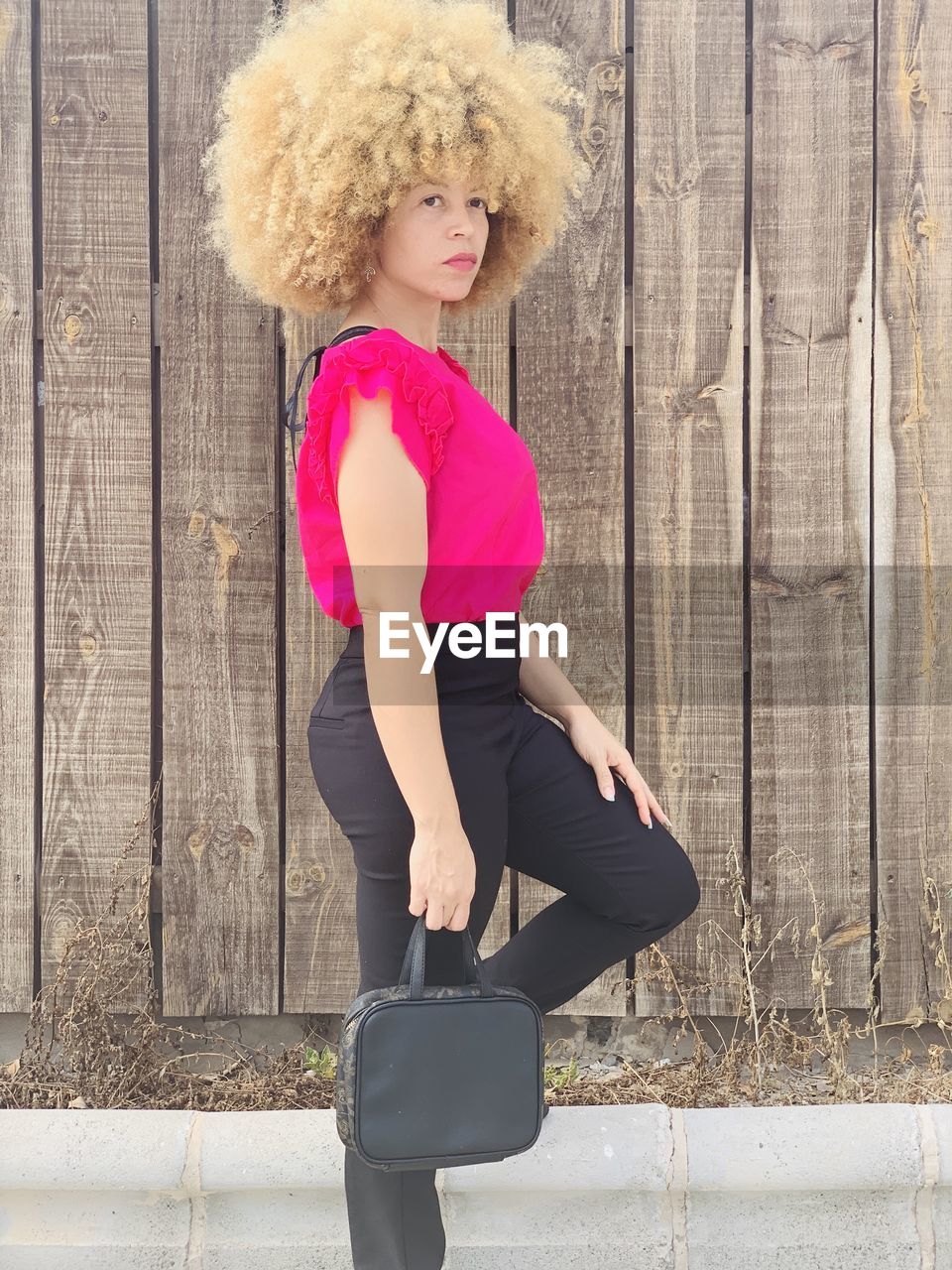 Side view of woman with curly hair standing by wooden wall outdoors