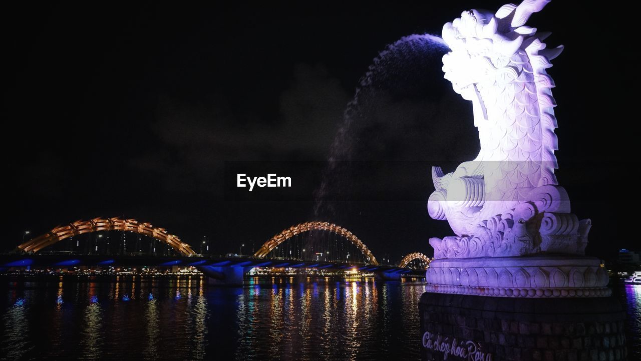 ILLUMINATED BRIDGE OVER RIVER IN CITY AT NIGHT