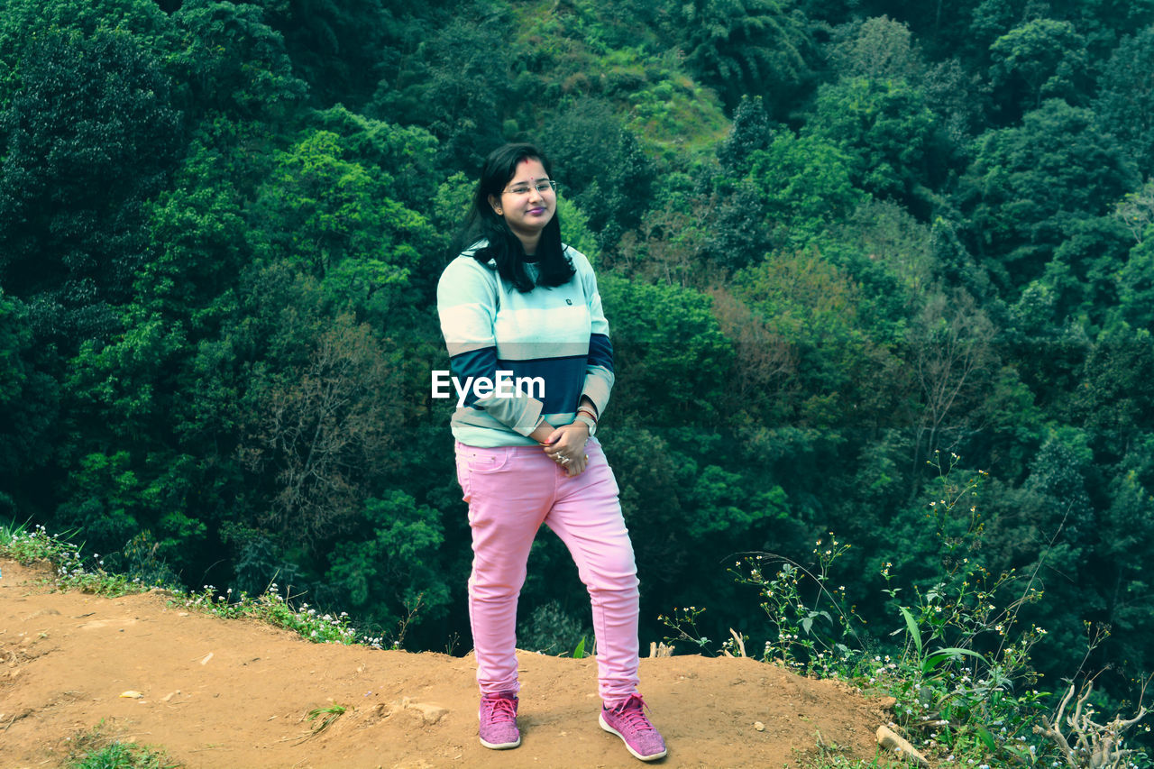 one person, full length, plant, lifestyles, tree, women, leisure activity, green, young adult, casual clothing, adult, nature, standing, land, front view, portrait, forest, smiling, day, female, beauty in nature, looking at camera, happiness, outdoors, emotion, walking, clothing, growth, sports, adventure, mountain, footwear, person