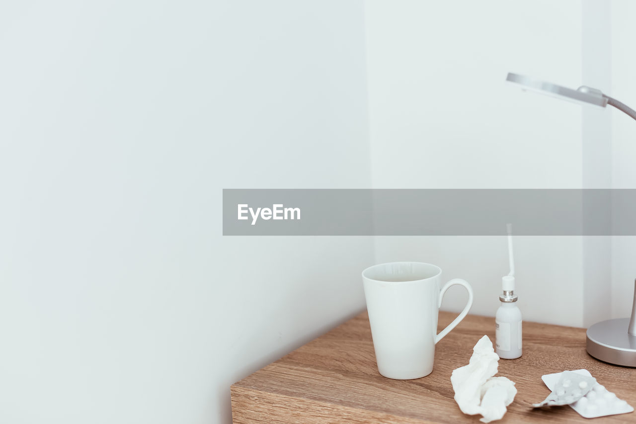 CLOSE-UP OF COFFEE CUP ON TABLE AGAINST WHITE WALL