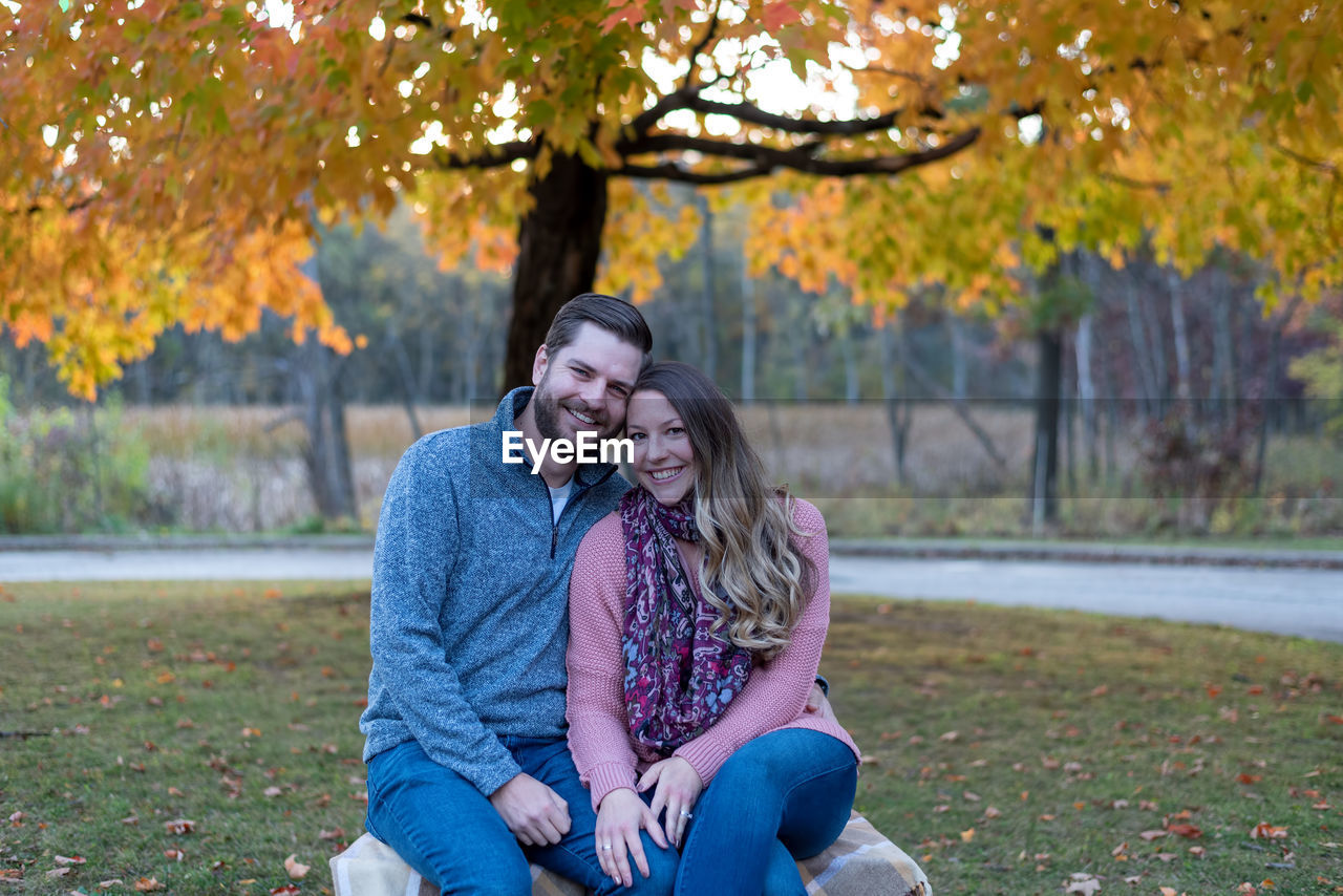 SMILING YOUNG WOMAN SITTING ON AUTUMN TREE