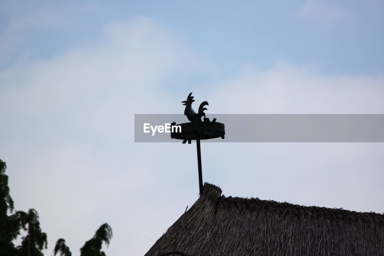 Low angle view of weather vane on rooftop against sky