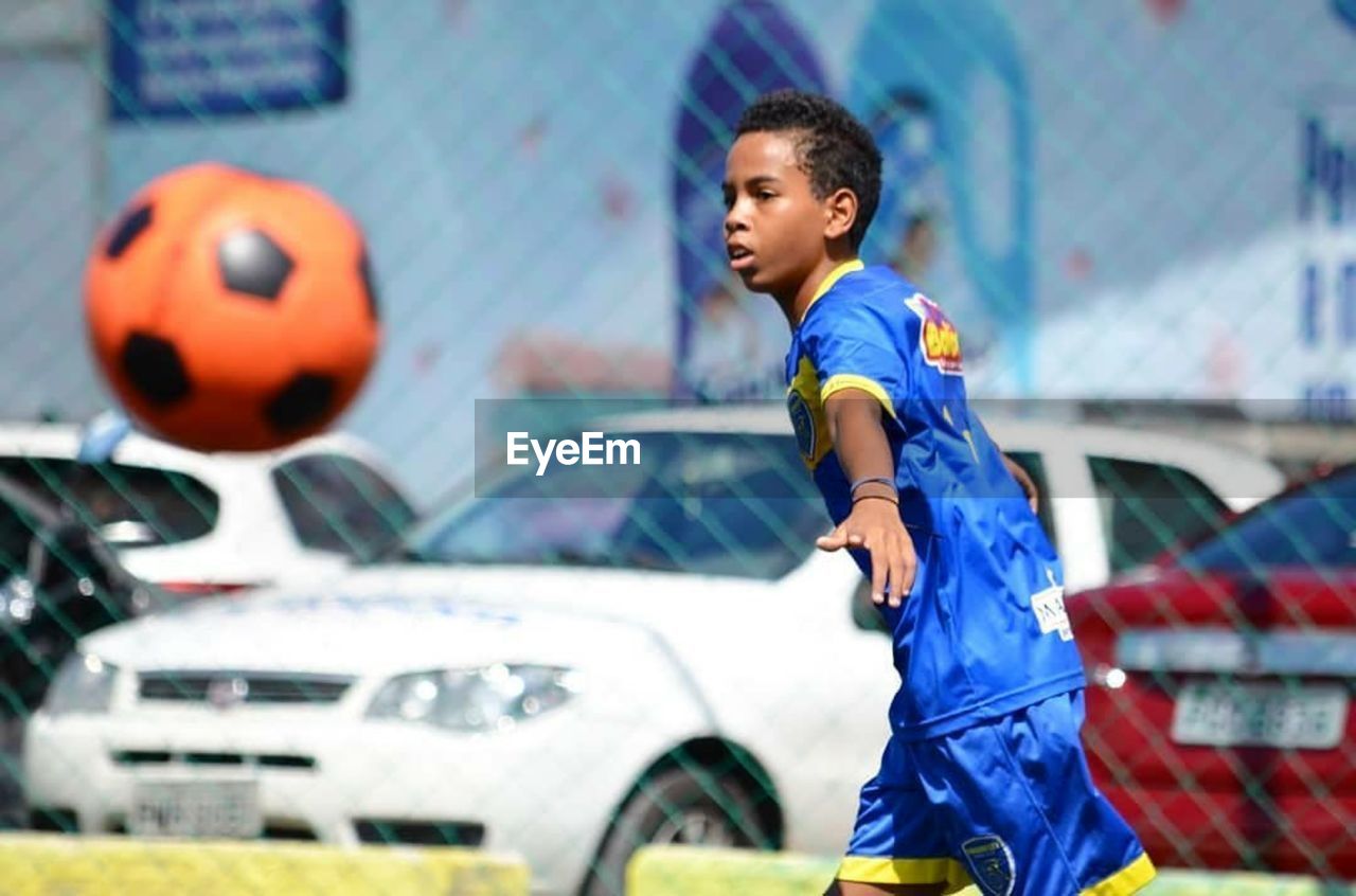 SIDE VIEW OF BOY STANDING BY CAR ON BLUE ROAD