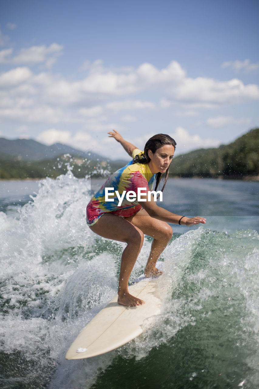 FULL LENGTH OF SHIRTLESS MAN SPLASHING WATER AGAINST SKY