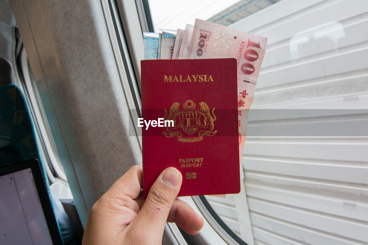 Cropped hand holding malaysian passport with paper currency in train