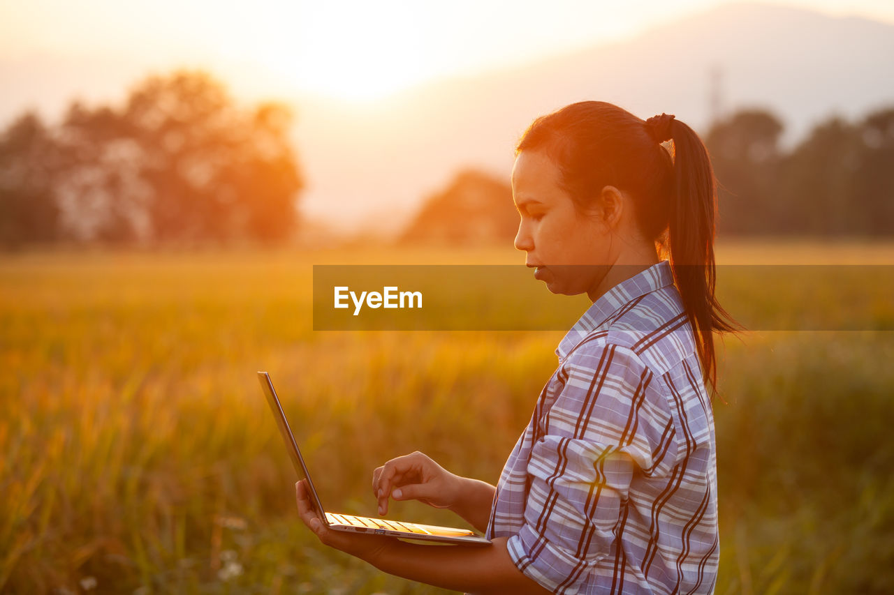 Side view of woman using laptop by plants