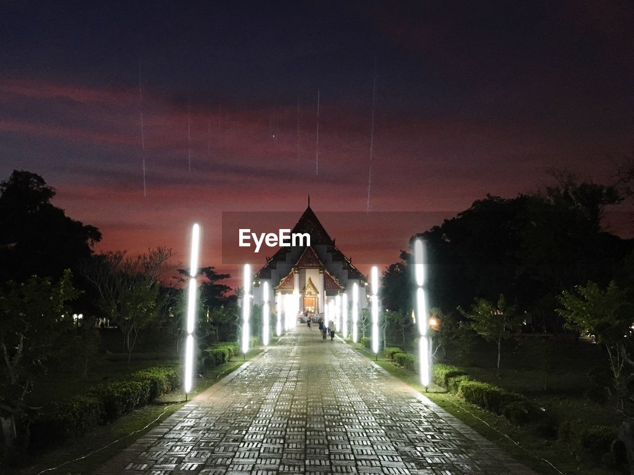 Footpath leading towards historic temple against sky during sunset