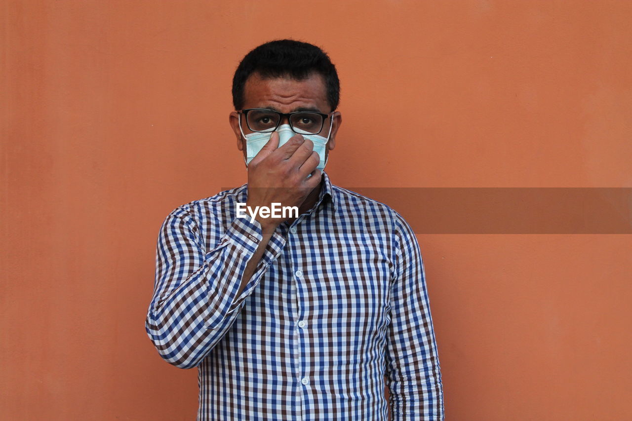 Portrait of man setting mask  standing against orange background