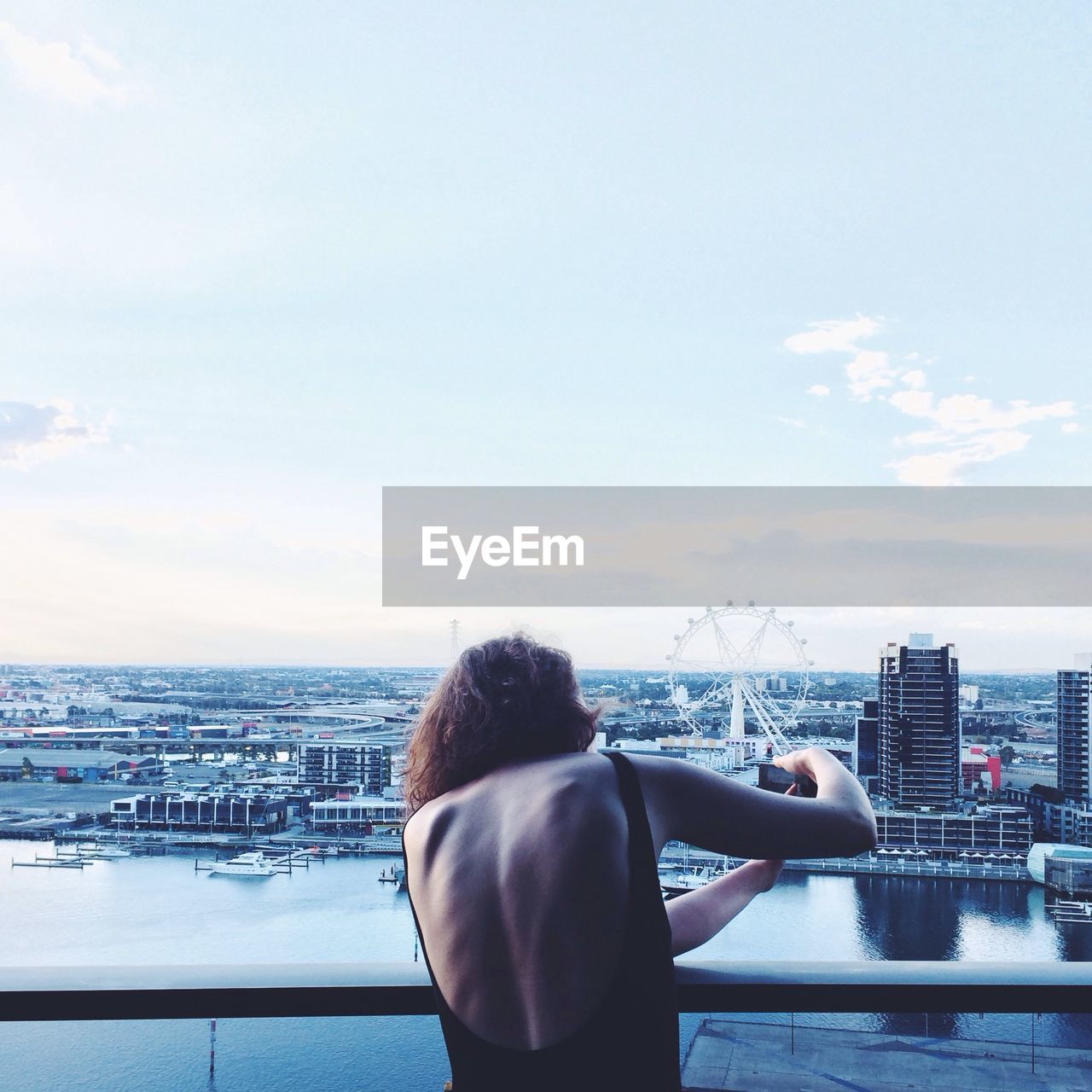 Rear view of woman photographing cityscape against sky