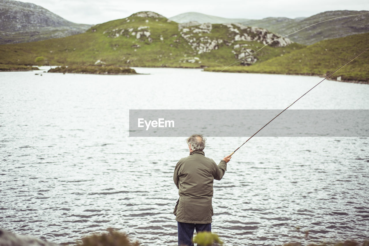 Man fly fishing by loch in remote mountains in scotland