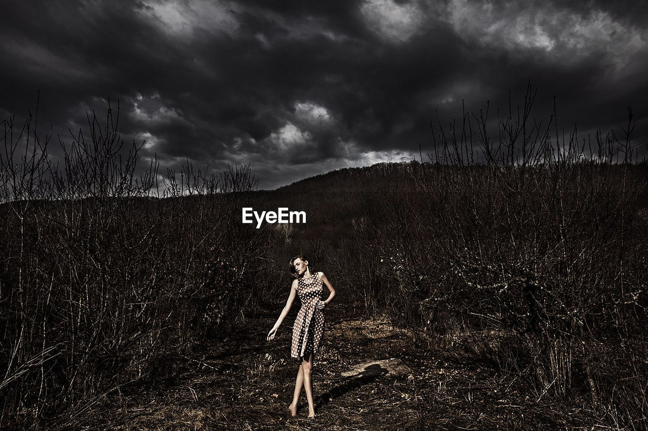 Woman standing on field against dark cloudy sky