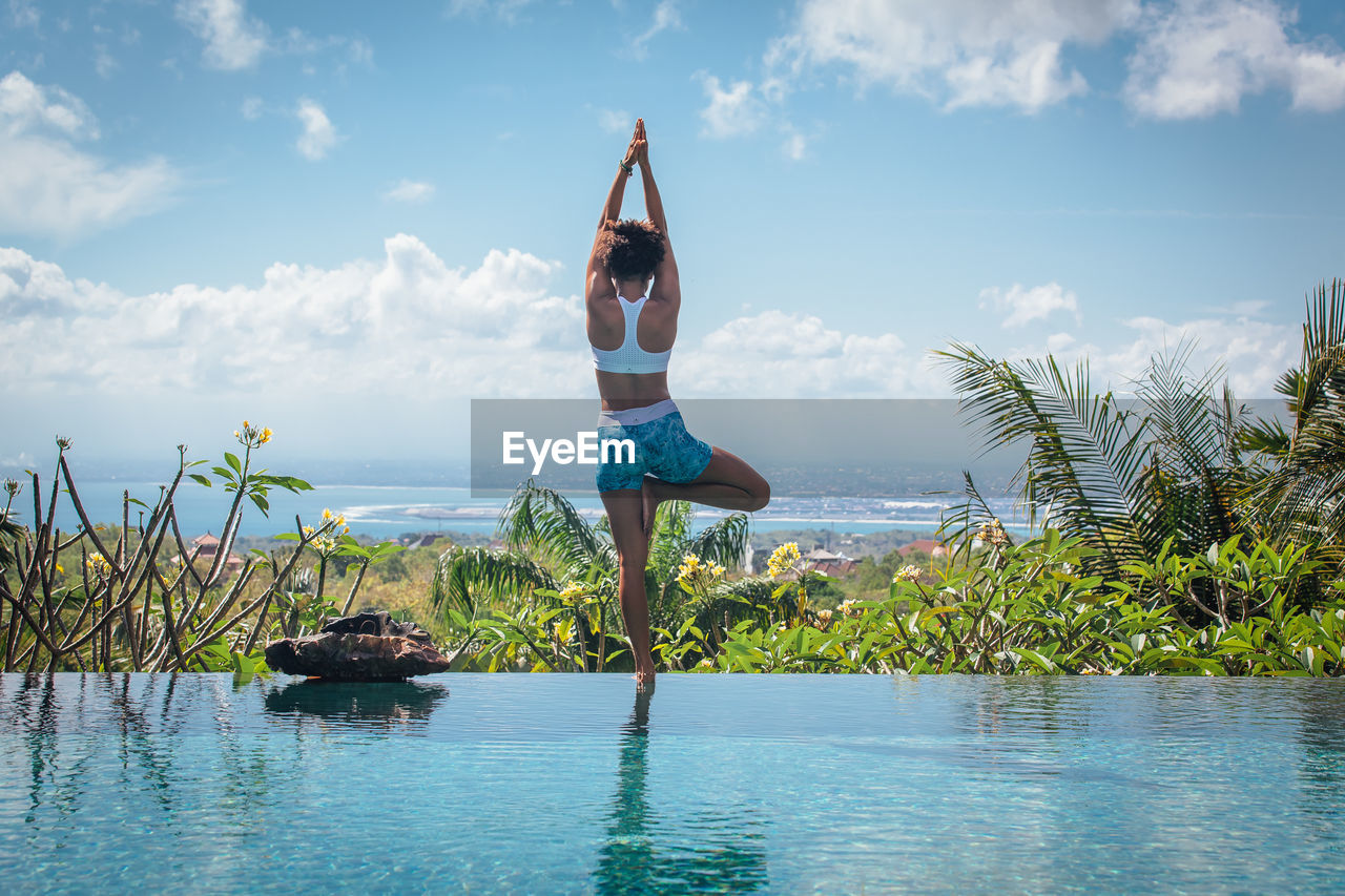 Rear view of young woman with arms raised standing by infinity pool