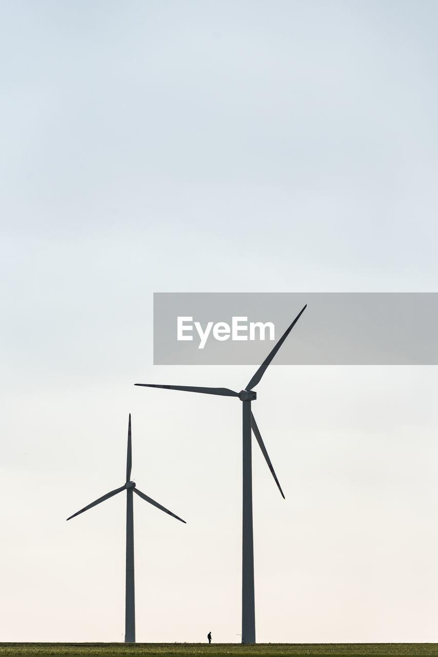 Two wind farms and a human silhouette showing the scale of windmill and man. 