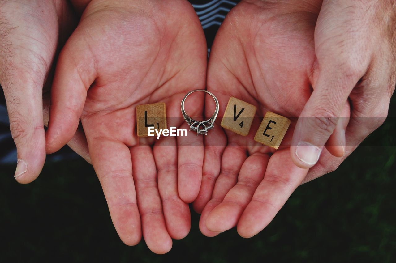 Cropped hands of couple holding wooden blocks with engagement ring making love text