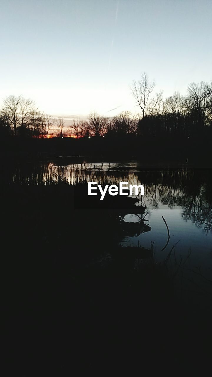 REFLECTION OF SILHOUETTE TREES IN LAKE AGAINST SKY